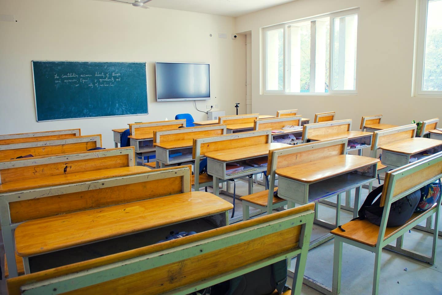 Empty modern classroom with wooden desks and chalkboard.