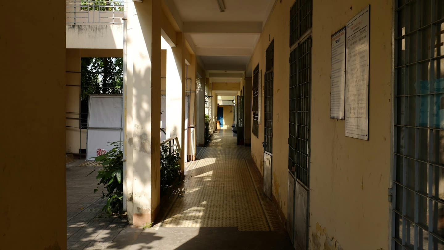 Person walking down a long sunlit school hallway.